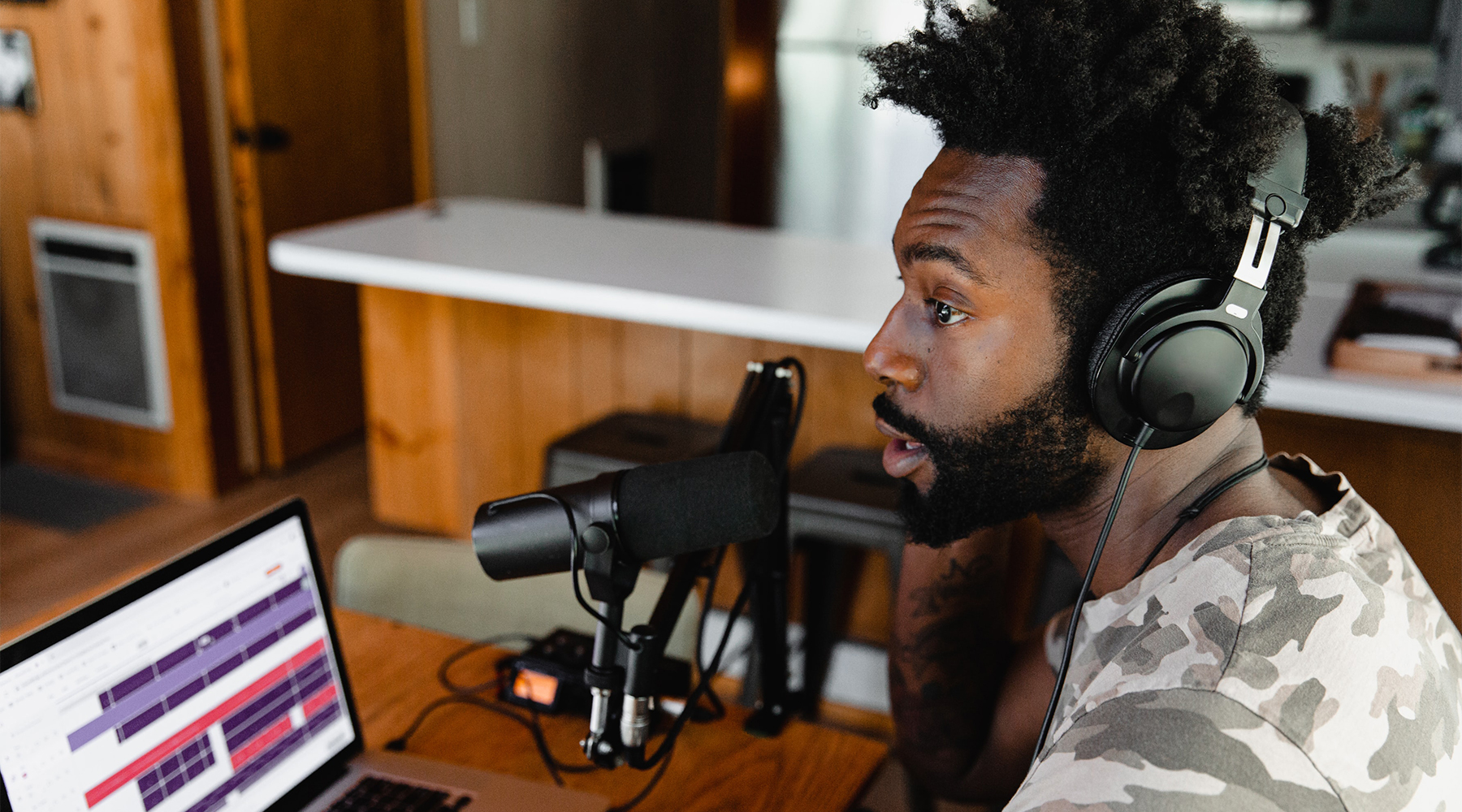 Person at desk speaking into studio mic with laptop nearby