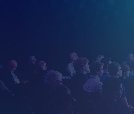 Audience in dark room staring off camera towards stage