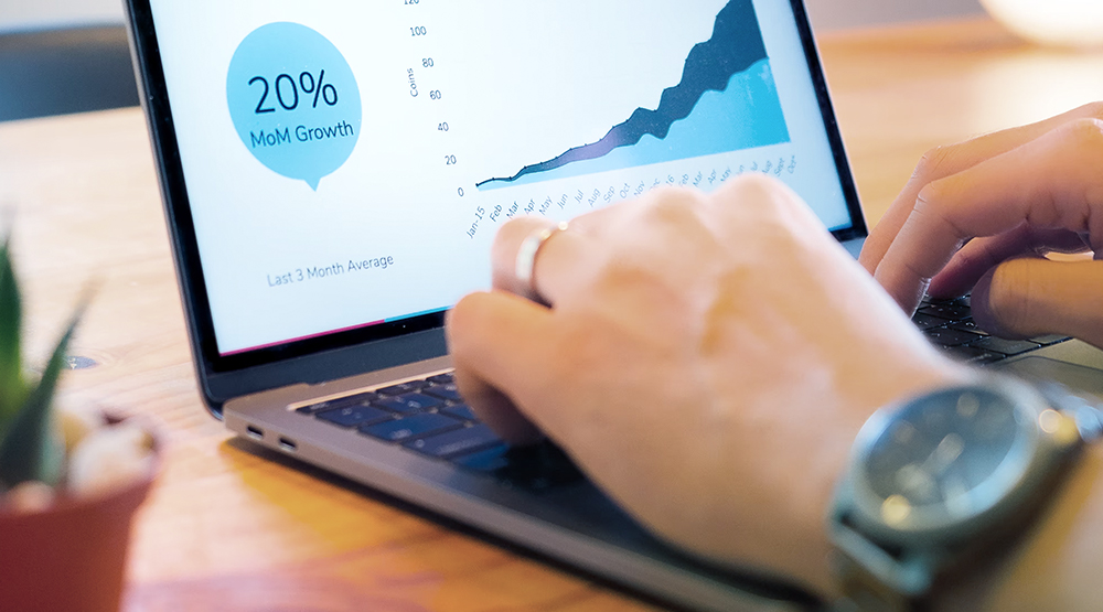 Close up of hands at laptop keyboard with chart going up shown on screen