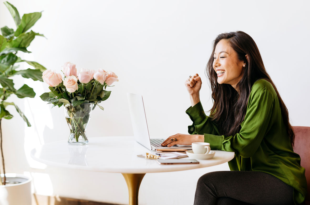 Woman smiling and working on a laptop with a vase of pink roses on her table