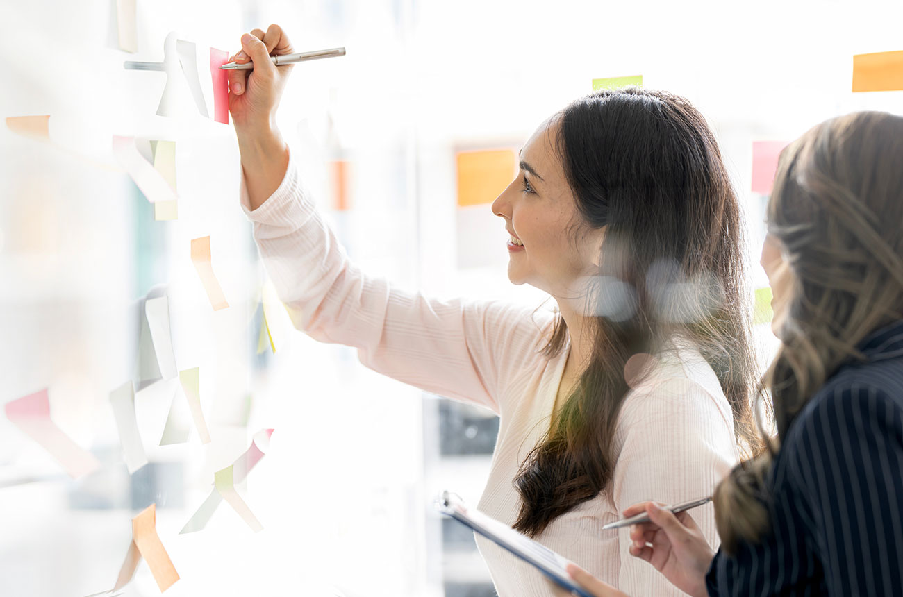 Person in white sweater posting sticky notes during a collaborative planning session
